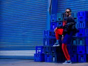 Stylish man posing in vibrant urban setting with colorful crates and shutters.