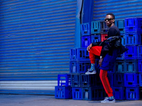 Stylish man posing in vibrant urban setting with colorful crates and shutters.
