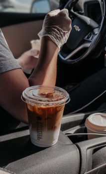 Close-up of iced coffee cup inside car with driver wearing protective gloves.