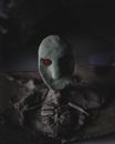 Creepy oval face with red eye over old bones on table in darkness