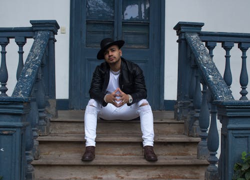 Man in Black Leather Jacket and White Pants Sitting on Stairs