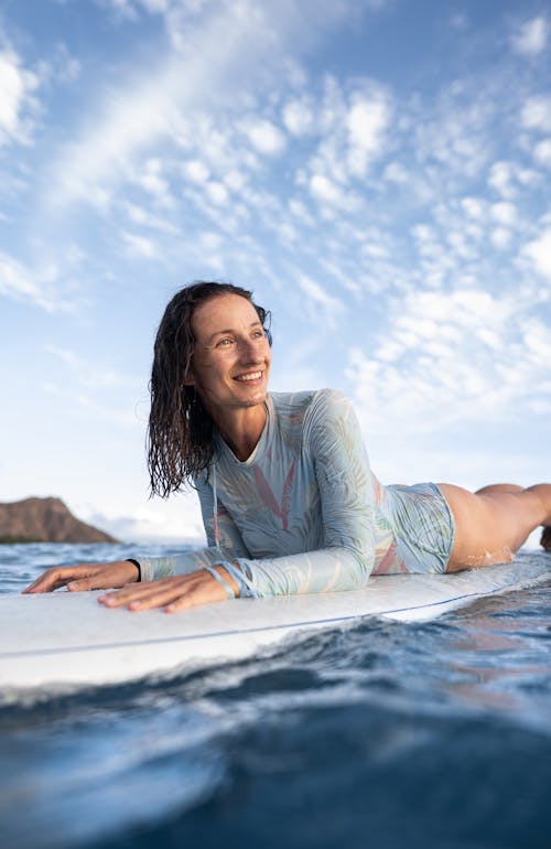 Happy young female traveler with wet hair lying on surfboard and looking away after training in wavy ocean on sunny day