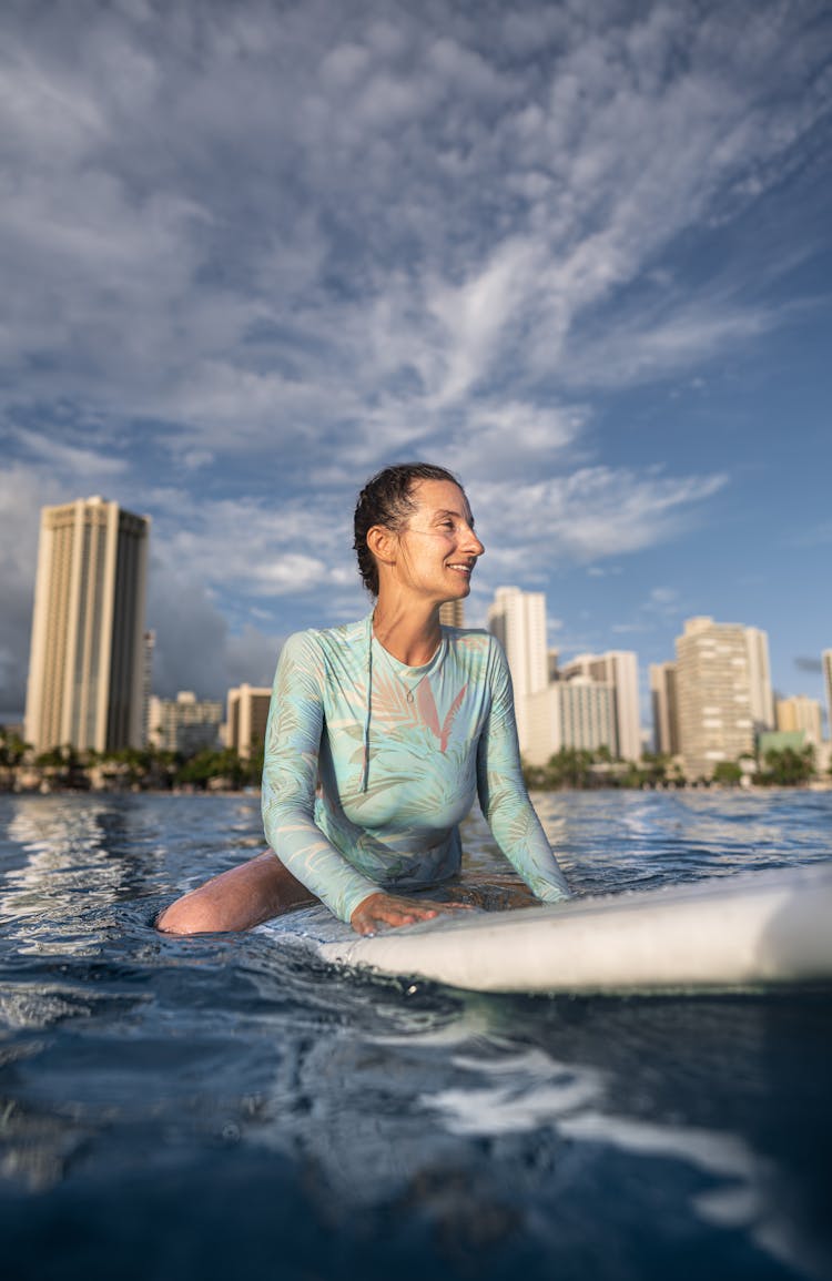 Happy Young Female Surfer Sitting On Board And Looking Away