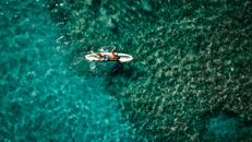 Anonymous male athlete floating in sea lying on surfboard