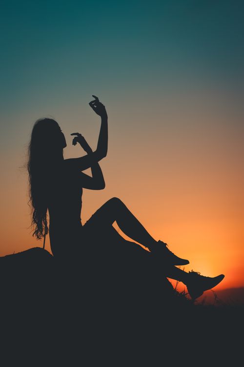 Free Silhouette of a woman sitting with graceful hand gestures during sunset creating a tranquil scene. Stock Photo