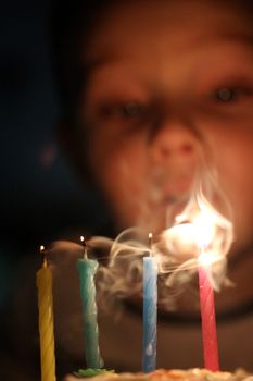 A child blowing out four colorful birthday candles creating a soft, dreamy smoke effect.