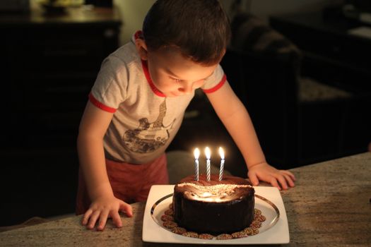 A young child blowing out birthday cake candles indoors, capturing a charming celebration moment.