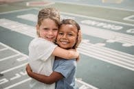 Smiling Girl in White Shirt Hugging Smiling Girl in Blue Denim Shorts