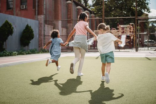 Three kids running joyfully on a sunny playground, embodying happiness and childhood fun.