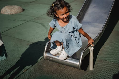 A Girl in Blue Dress Sitting on the Edge of a Slide