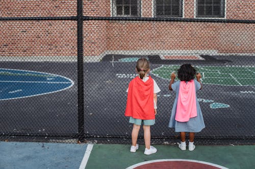 Children with a Pink and Red Capes Standing Beside the Chain Link Fence