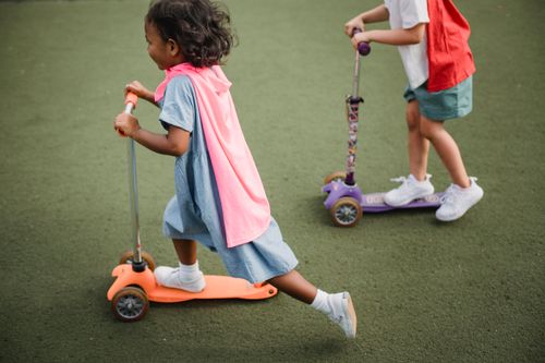 Free Children enjoying a fun ride on kick scooters outdoors. Vibrant and playful scene. Stock Photo