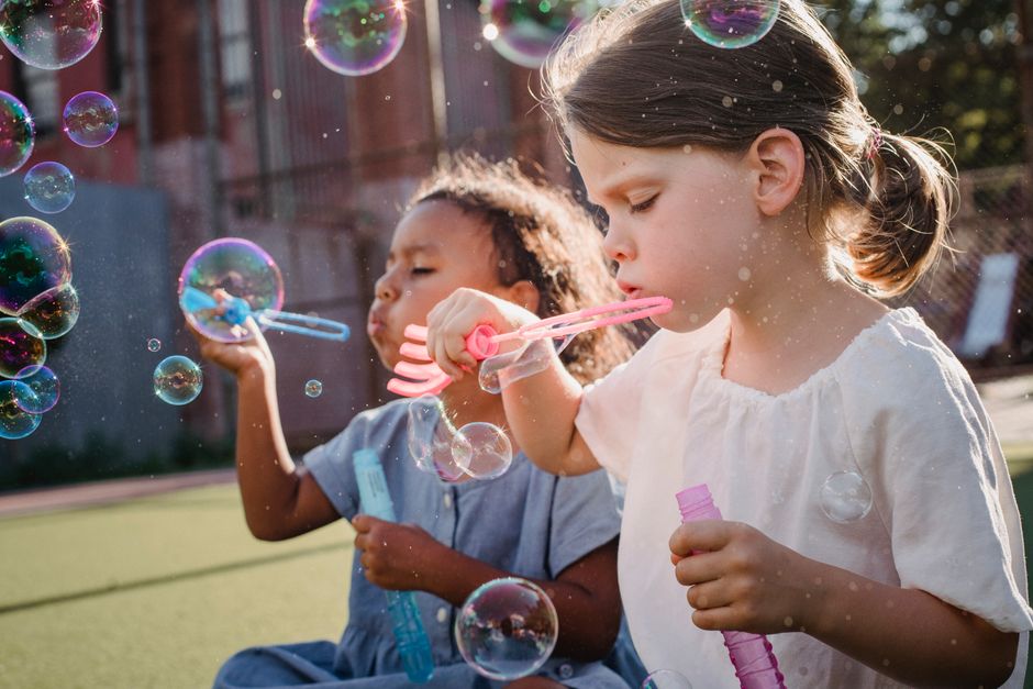 Two young girls joyfully blowing bubbles in the sunshine outdoors.