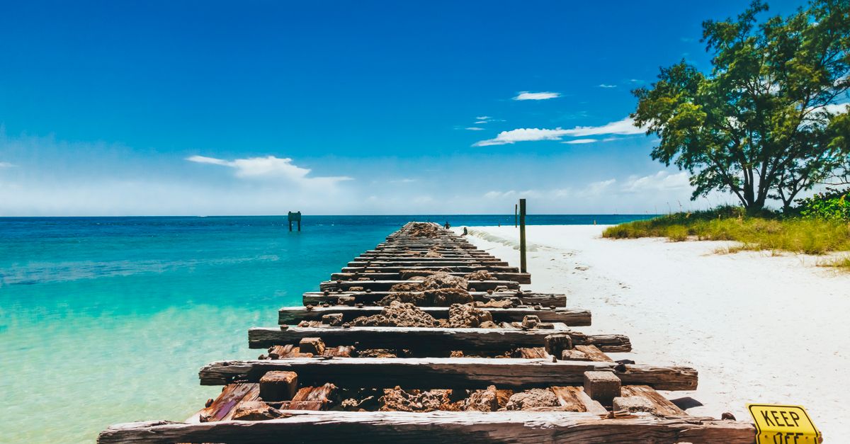 A sunny day at Bradenton Beach, FL, showcasing a wooden jetty leading into clear turquoise waters.