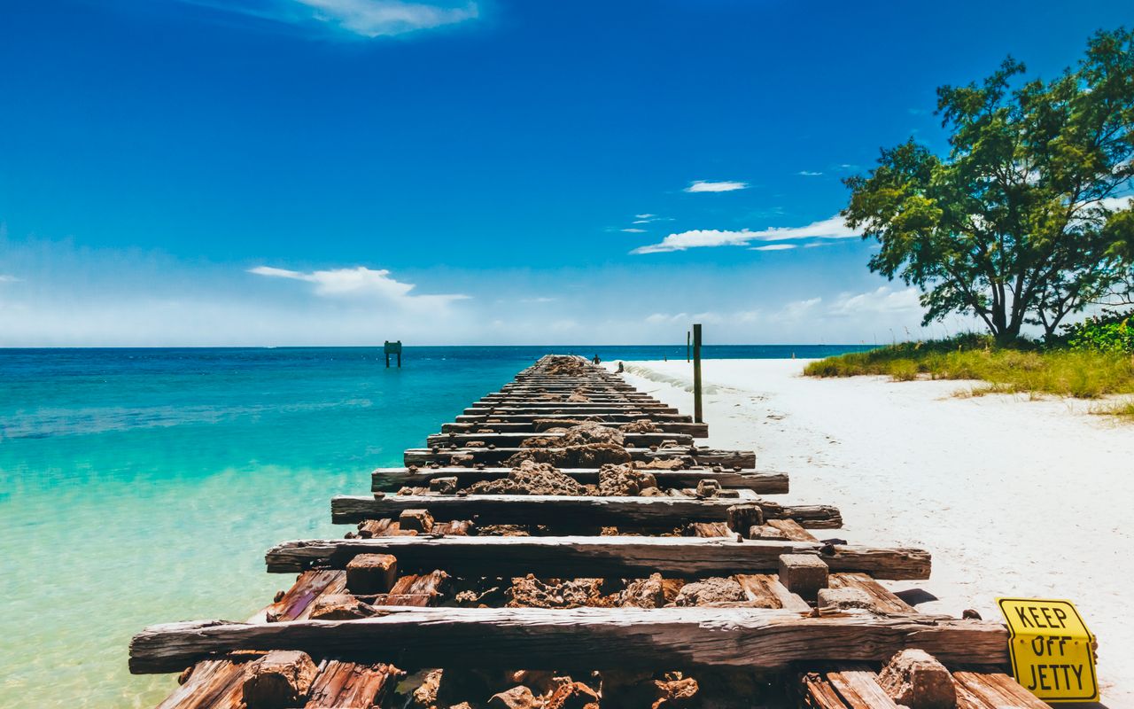 A sunny day at Bradenton Beach, FL, showcasing a wooden jetty leading into clear turquoise waters.