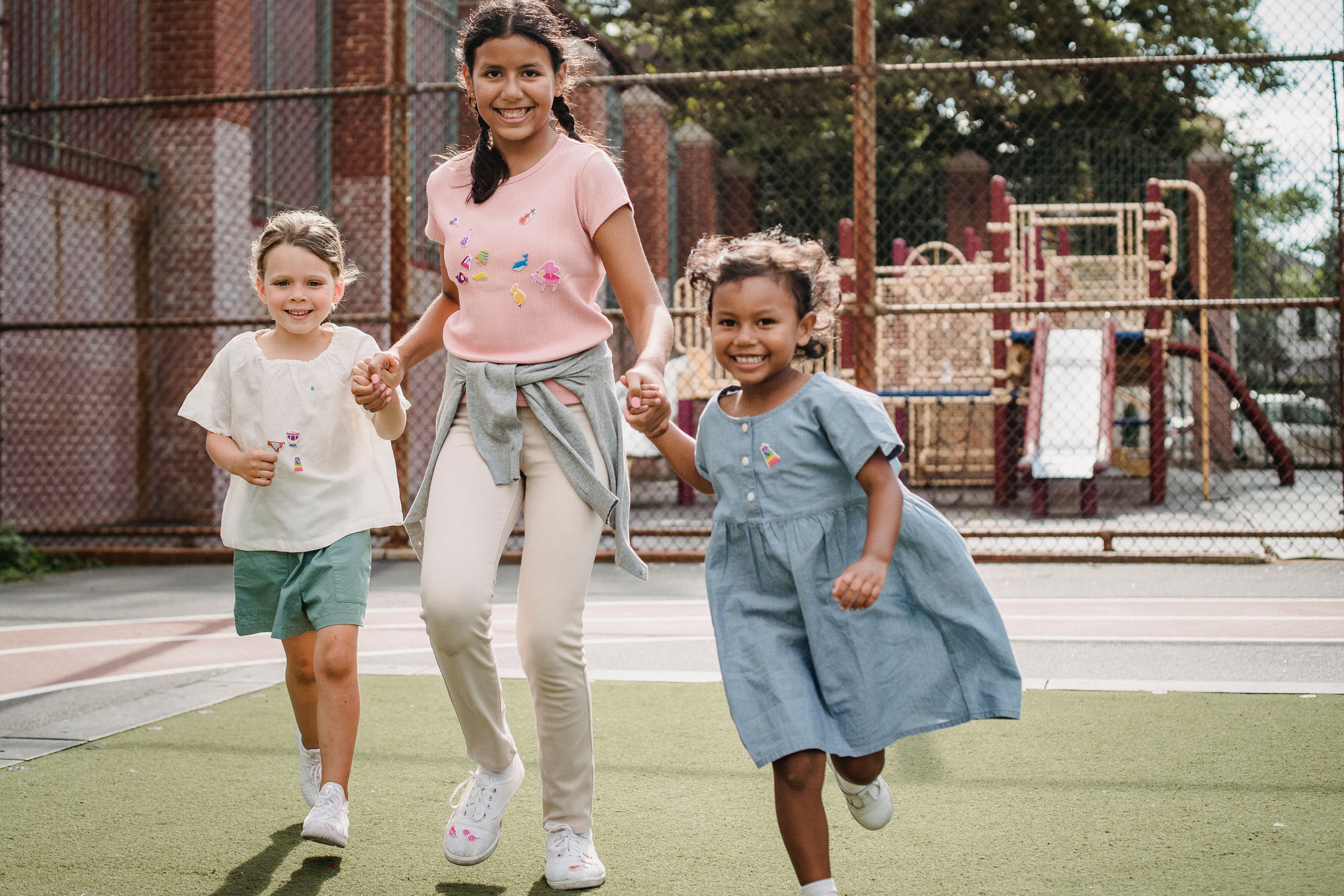 Three happy children holding hands and running together on a playground.