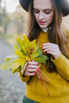 Chic young woman with fall leaves, showcasing autumn style outdoors.