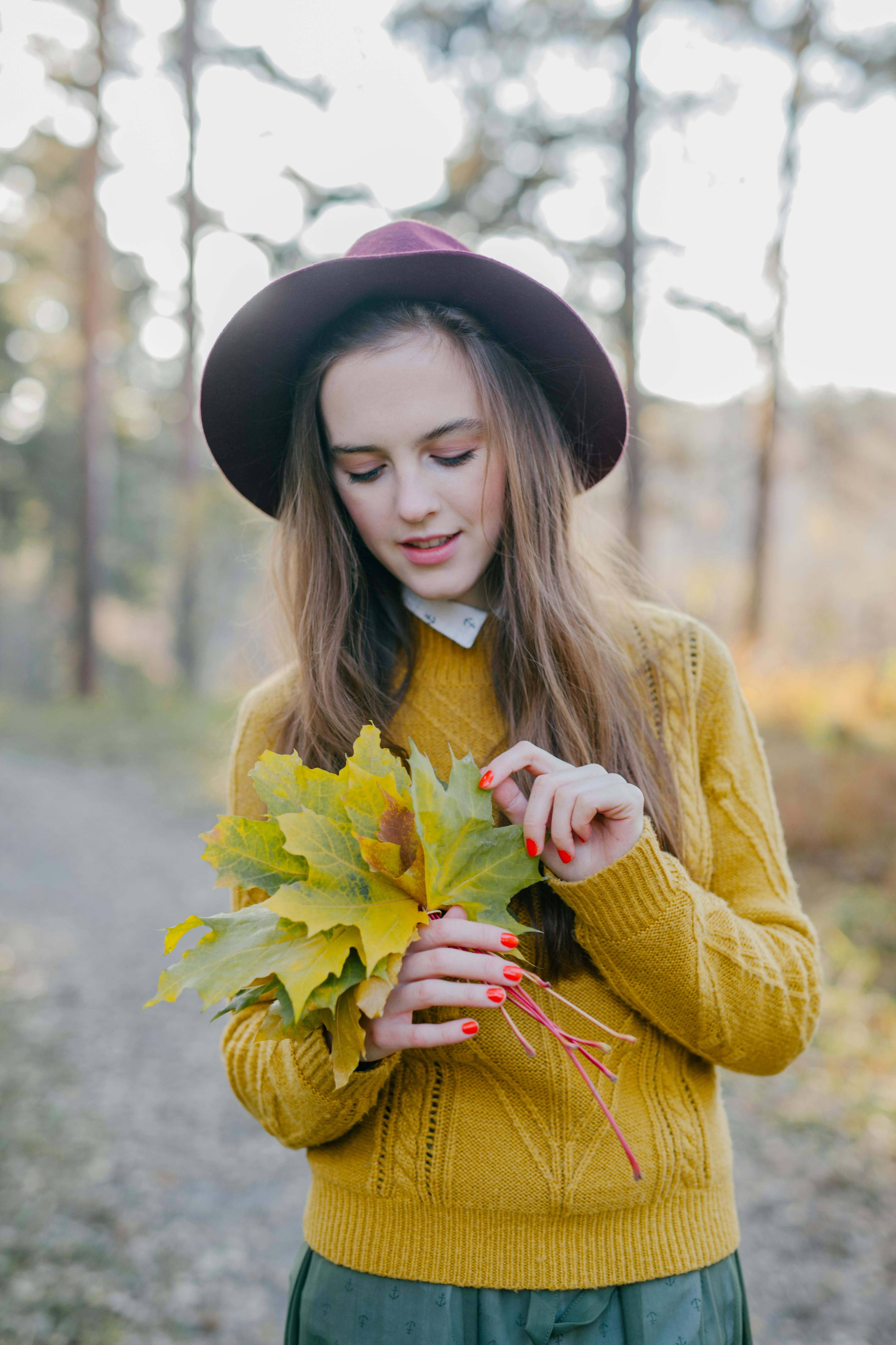 一位穿着芥末色毛衣的女人在森林中拿着秋叶