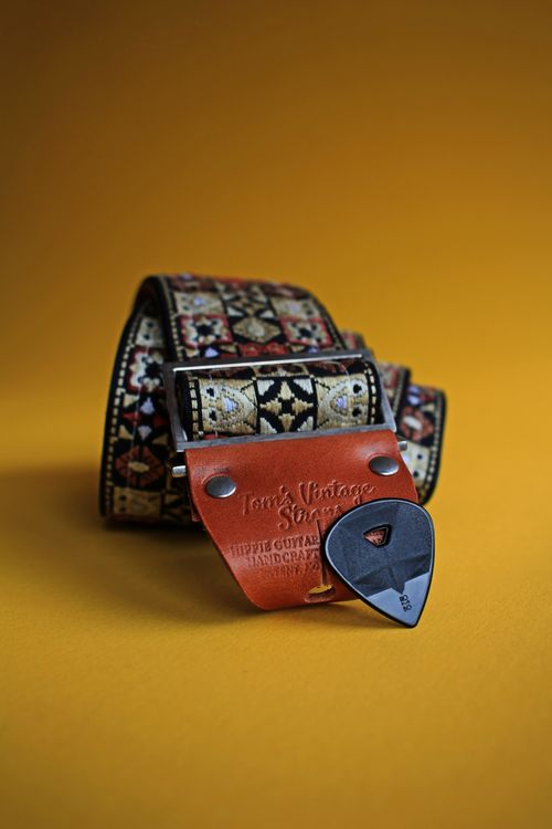 Free Artistic shot of a decorative guitar strap with an engraved pick on a warm yellow backdrop. Stock Photo