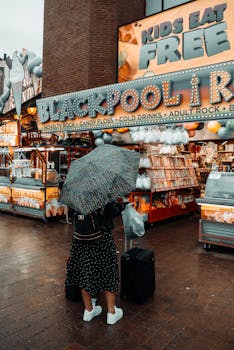 Woman with umbrella and luggage browsing a Blackpool rock shop in rainy weather.