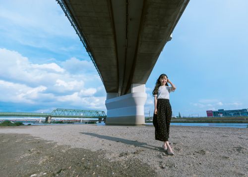 Free A young Asian woman smiling while standing under a large city bridge on a sunny day. Stock Photo