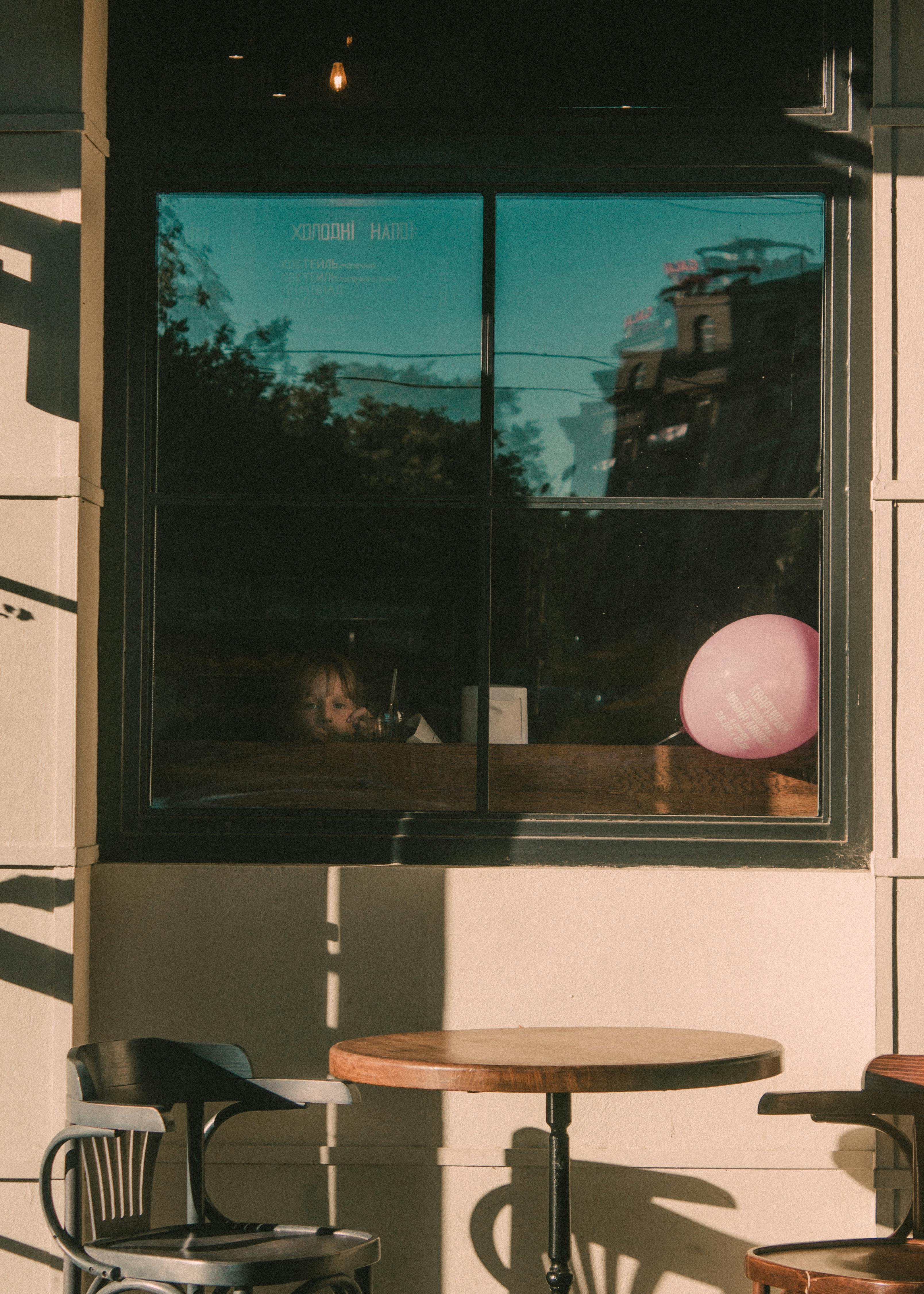 A child looks out from a window with a balloon, capturing a serene street moment.