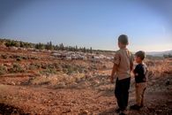 Back view full body of ethnic homeless kids standing on dry ground with tents at distance