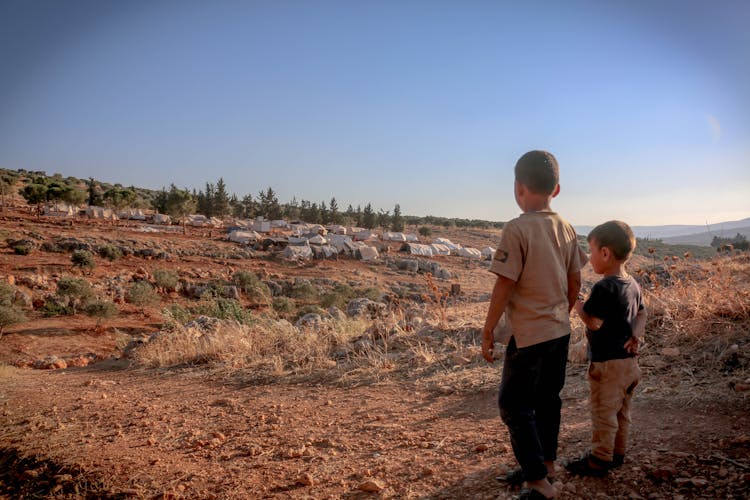 Ethnic Boys Standing In Steppe With Refugee Camp