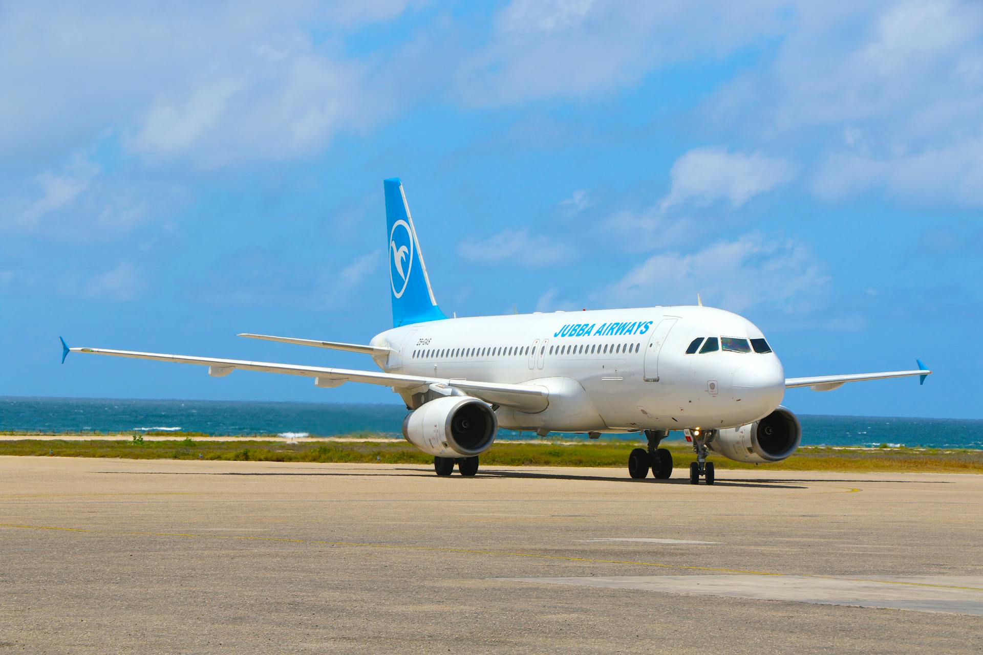 Jubba Airways airplane parked at Mogadishu airport on a bright day, with ocean view in the background.
