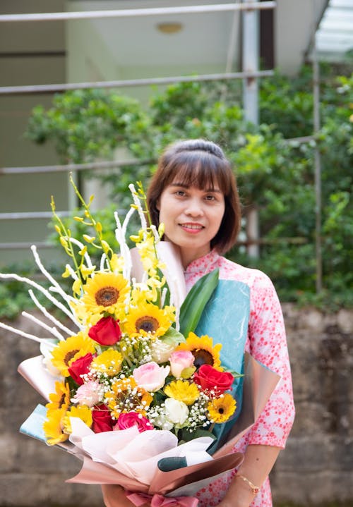 Woman in Pink and White Floral Shirt Holding a Bouquet of Flowers