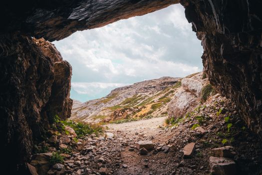 Rocky cave entrance overlooking mountainous landscape in Italy's Tre Cime di Lavaredo.