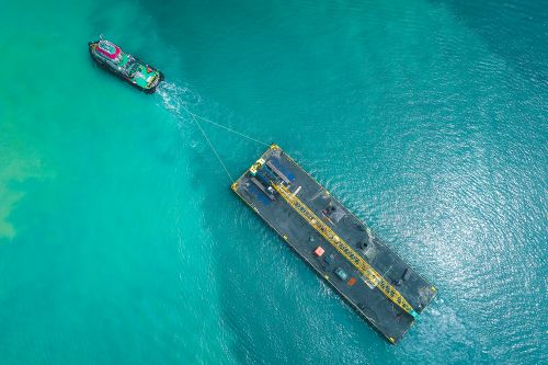 Free Drone view of contemporary powerful boat pulling swimming platform with crane along blue calm seawater Stock Photo