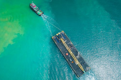 Aerial view of modern powerful motorboat floating on azure seawater and transporting big platform with crane