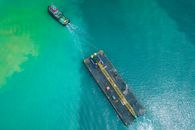 Aerial view of modern powerful motorboat floating on azure seawater and transporting big platform with crane