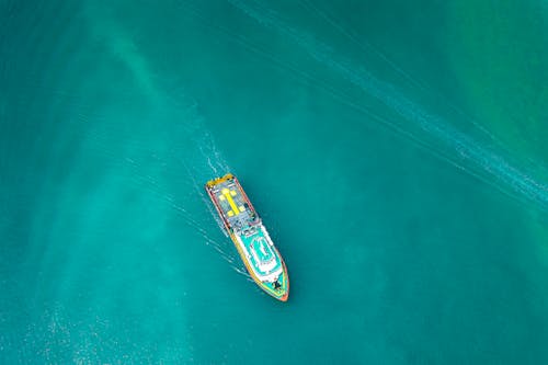 Aerial view of contemporary industrial boat floating along turquoise rippling ocean on clear day