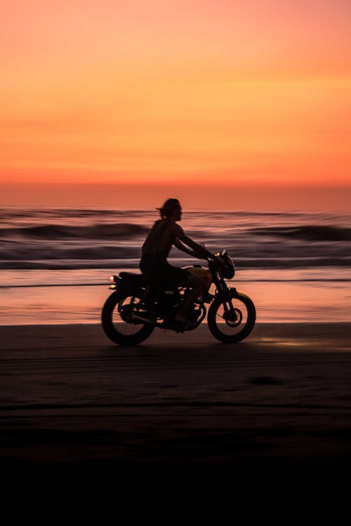 Man Riding Motorcycle Sur La Plage Pendant Le Coucher Du Soleil