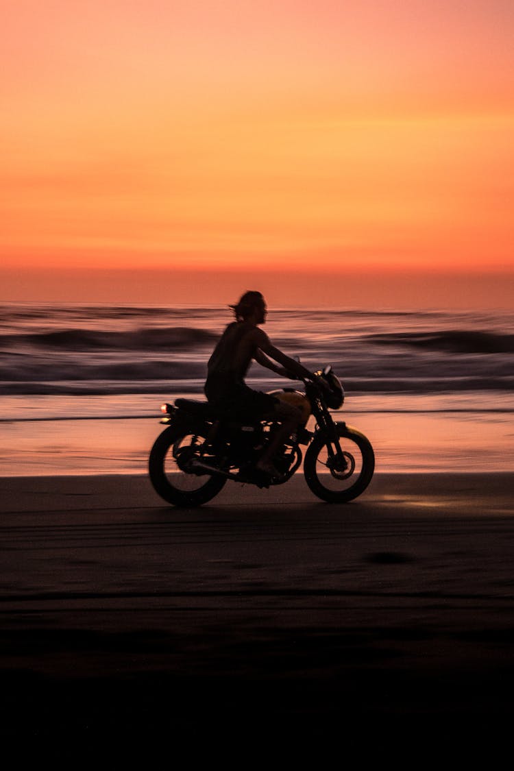 Man Riding Motorcycle On Beach During Sunset