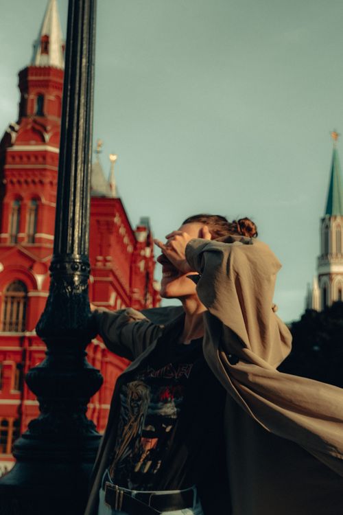 Free Young female in trendy outfit standing on street and hiding face behind hand at daylight Stock Photo
