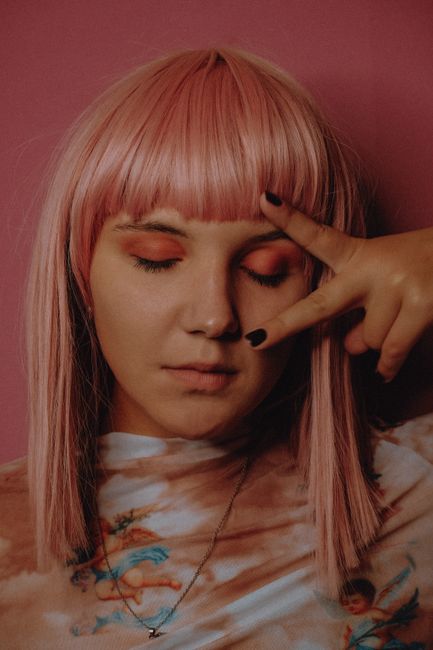 Portrait of attractive pink haired female with bright make up standing on vivid background and closing eyes