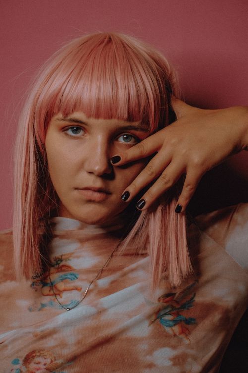 Free Portrait of pink haired female covering half of face with hand and looking at camera Stock Photo
