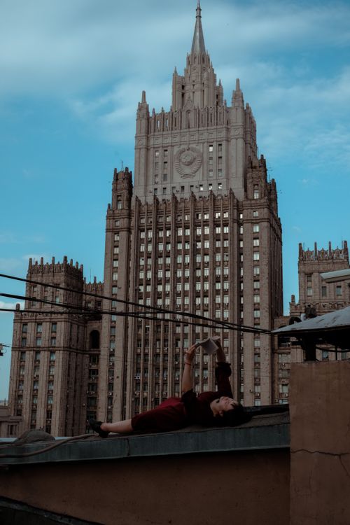 Free Full body of brown haired female lying on rooftop and reading book against classic building under blue sky Stock Photo