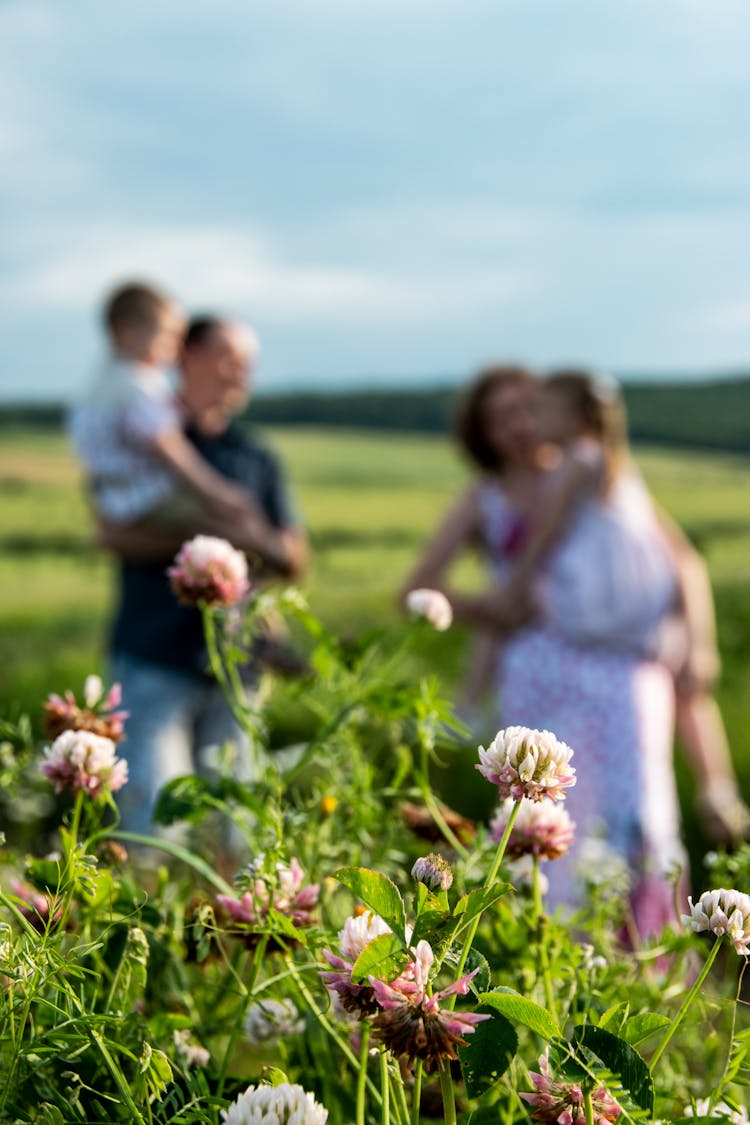 Family In Field With Clover Flowers In Foreground