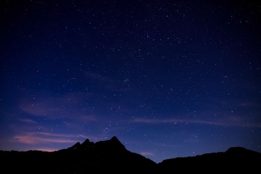 夜幕下，壮丽山脉的剪影映衬着黑暗的天空，高地上明亮的星星在自然中闪烁