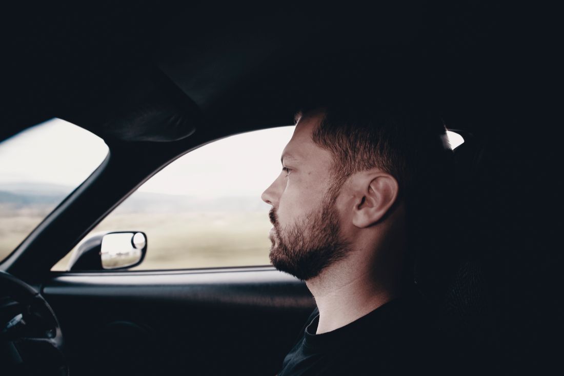 Side profile of a bearded man driving a car, focused and intent on the road
