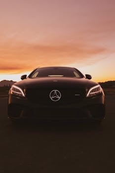 Front view of a luxury black car against a golden sunset sky, showcasing elegance.