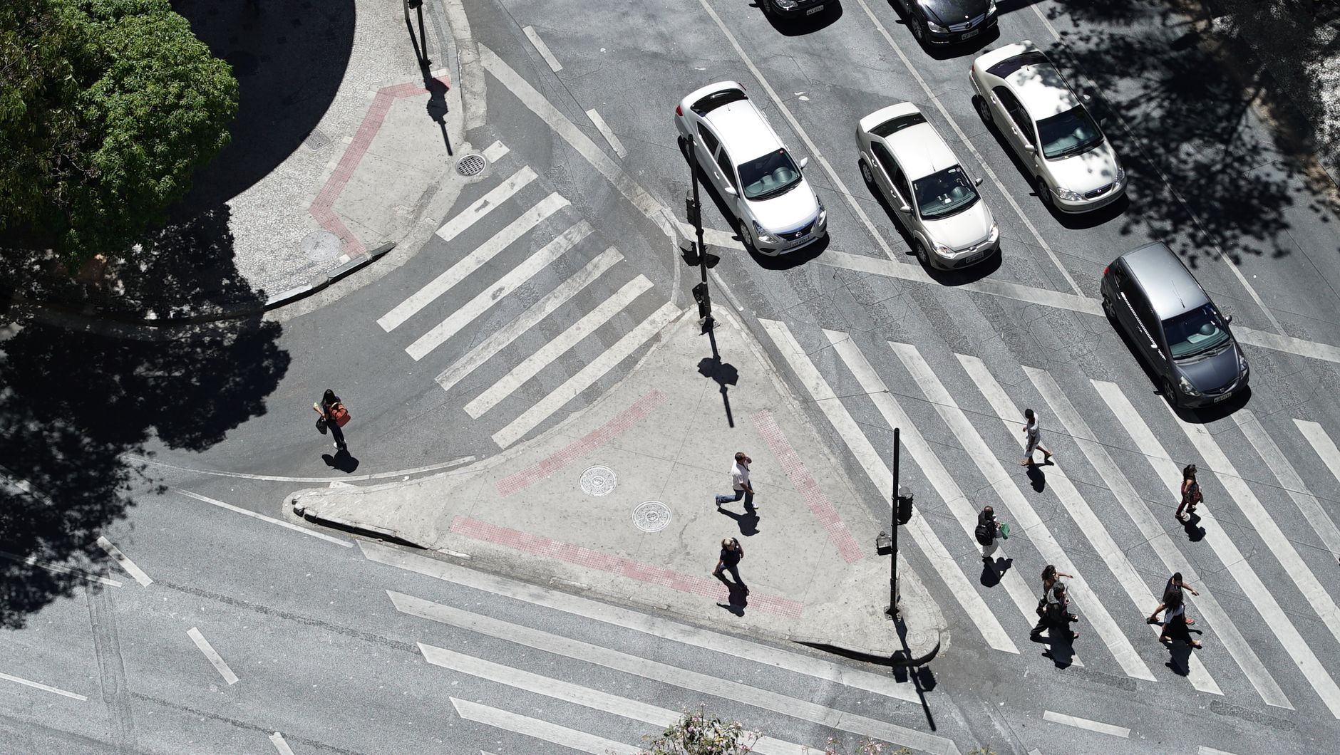 Top-down view of a busy pedestrian crossing in a city intersection with shadowed pedestrians and cars.