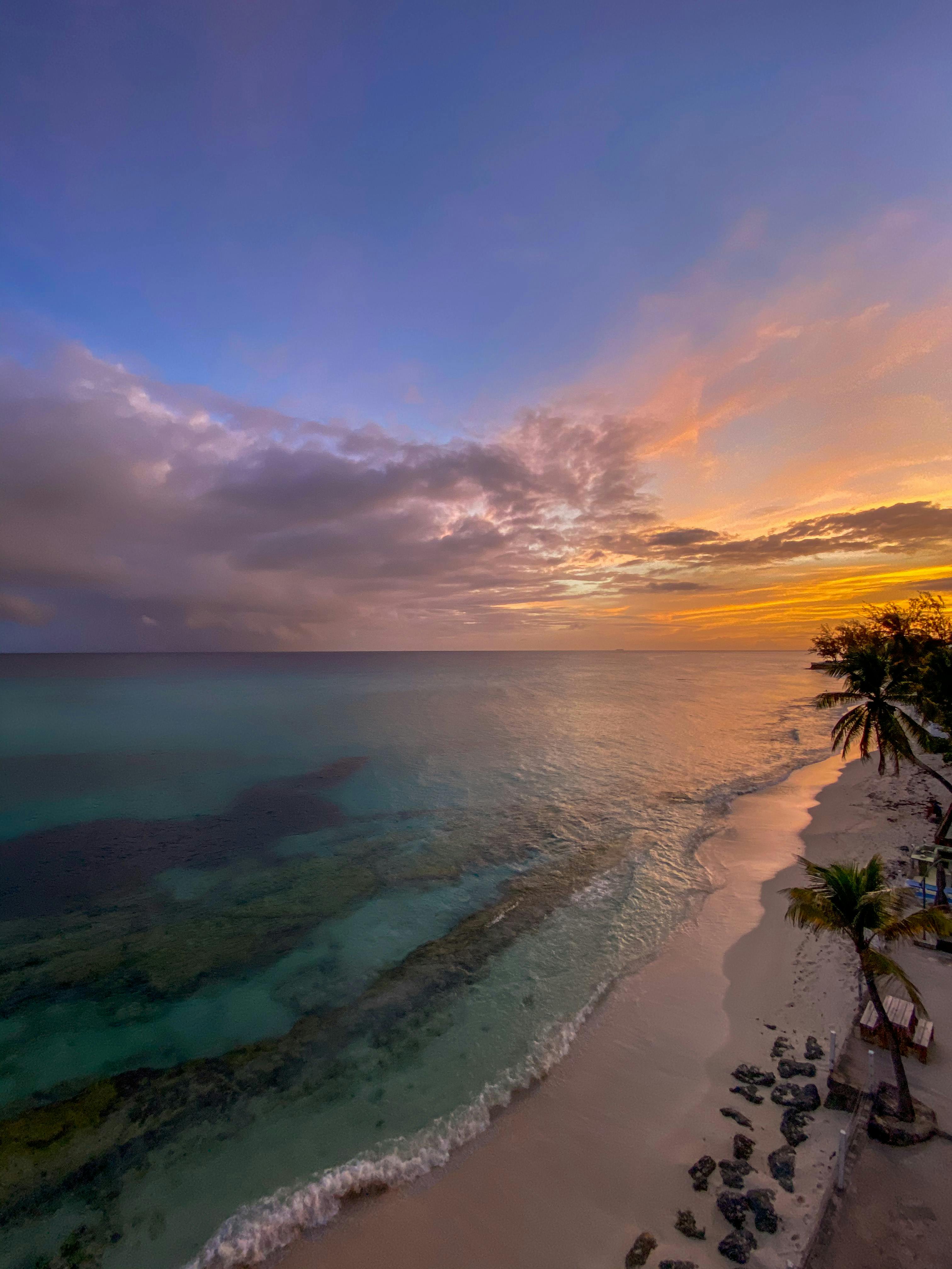 Aerial view of a tropical beach at sunset with vibrant colors and serene Caribbean waters.