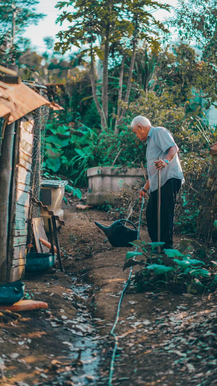 An Elderly Man Filling A Watering Can With Water