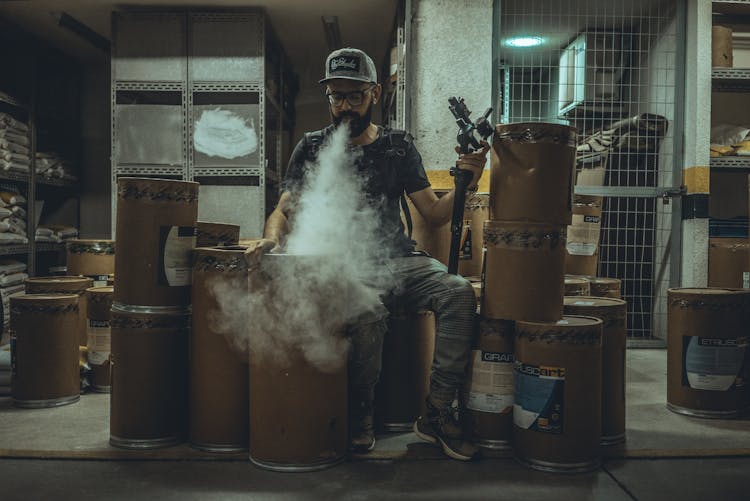 Man Blowing Smoke Sitting On Cardboard Containers