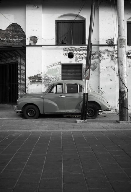 Black and white of vintage automobile on paved street near weathered house with brick elements on walls